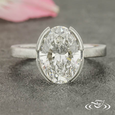An oval diamond is held in a milgrain bezel setting with four gaps in the bezel.