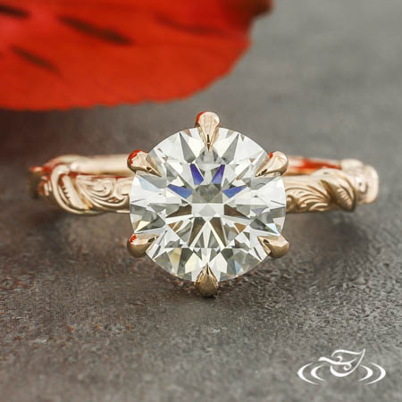 A round diamond in a six prong pointed setting with engraved band with filigree wire wrapped around the band.