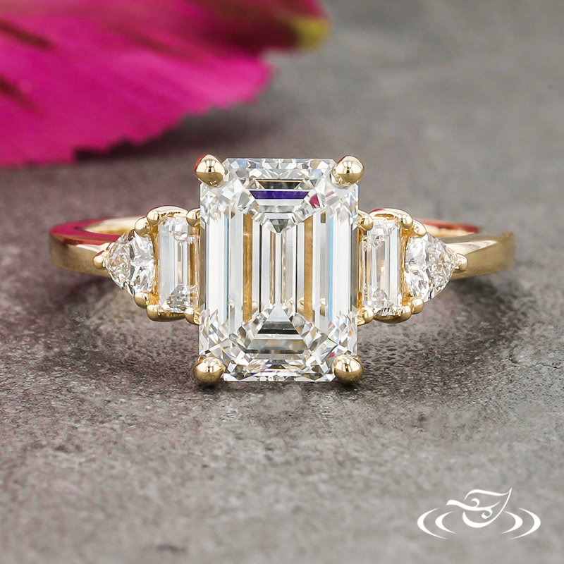 An emerald cut diamond with baguette and round diamond accents. This classic ring features a four prong setting and a yellow gold band.